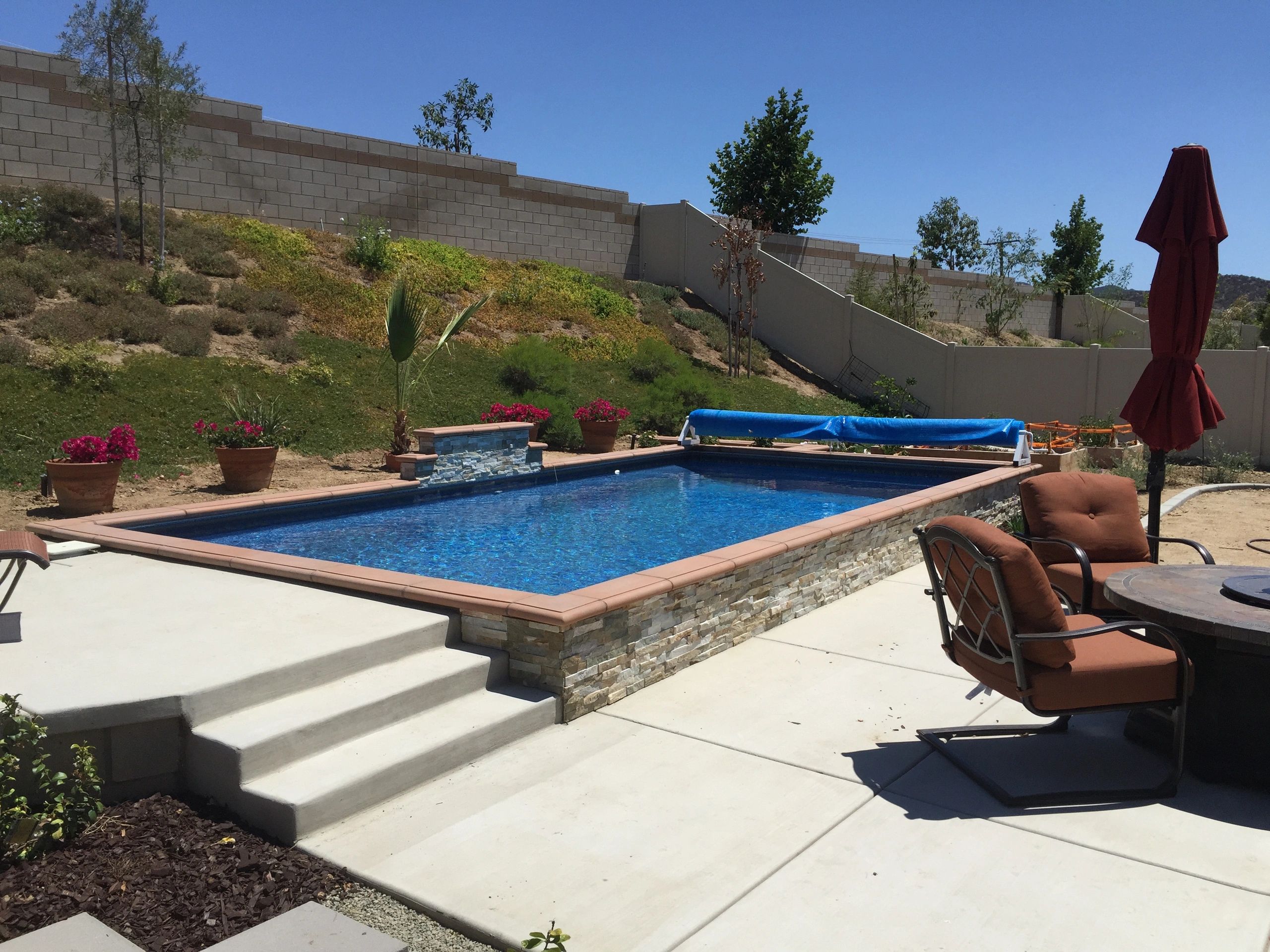 Completed in-ground vinyl pool with a raised stone water feature by Aqua Splash